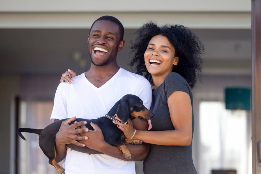 Happy-couple-stands-outside-home-with-adopted-dog