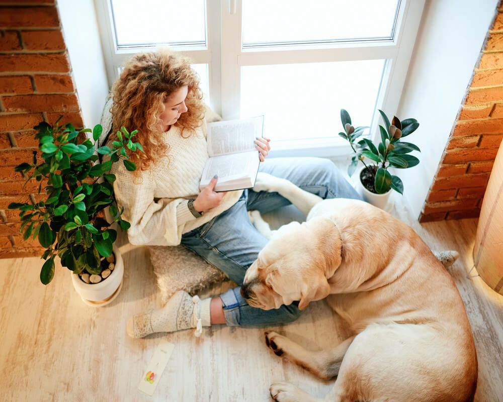 young-woman-catches-up-on-her-reading-while-dog-snuggles-up-at-her-feet