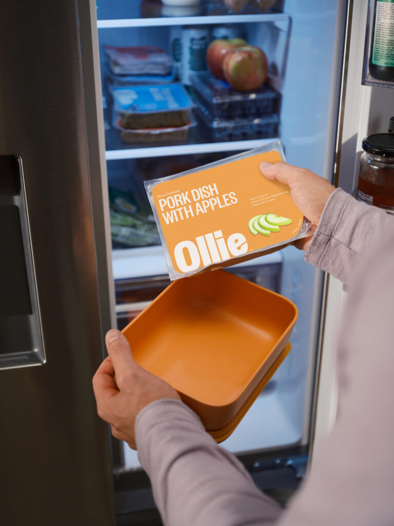 A man holding Ollie fresh Pork Dish with Apples in front of an open refrigerator