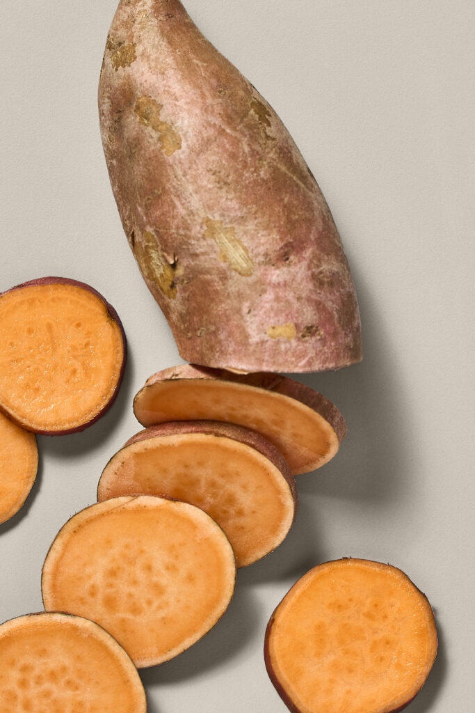 Half of a sweet potato arranged with slices of sweet potato on a beige background